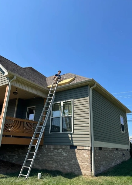 Nicodemus working on a roof, with a ladder against the house